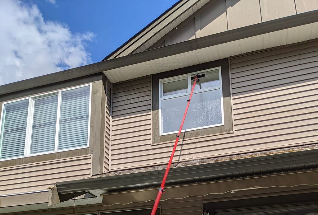 Cleaning windows using an orange pole to reach the second floor.