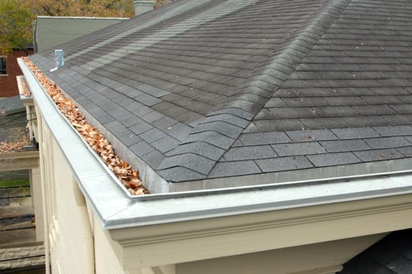 A house that is full of dried leaves on roof gutters.