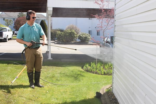 A man is wearing a light blue polo shirt while holding a pressure washer to clean the house.