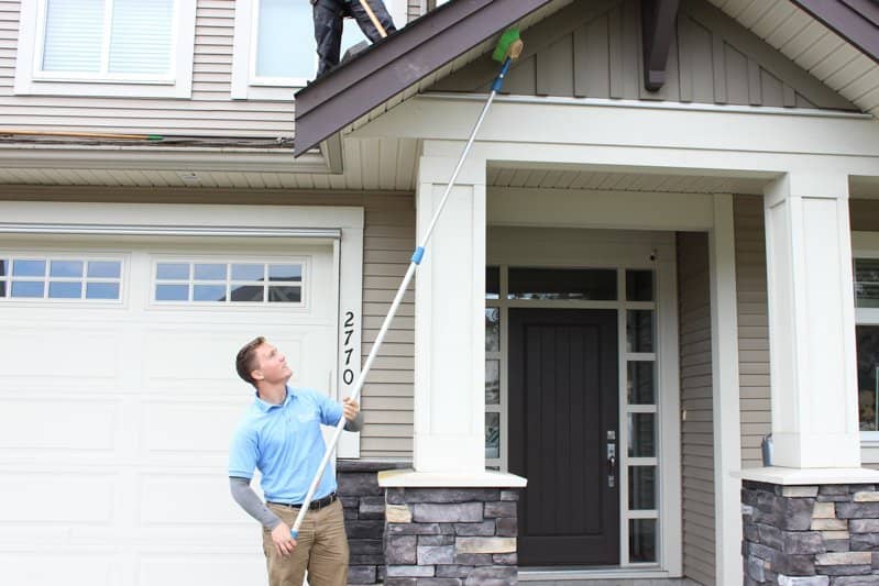 A man from fuse power washing wearing a sky blue polo shirt and holding a soffit brush to clean soffits.