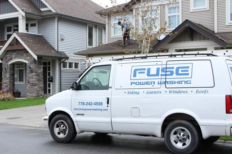 A van of Fuse Power Washing park side of the road, and A man was cleaning the roof behind the tree.