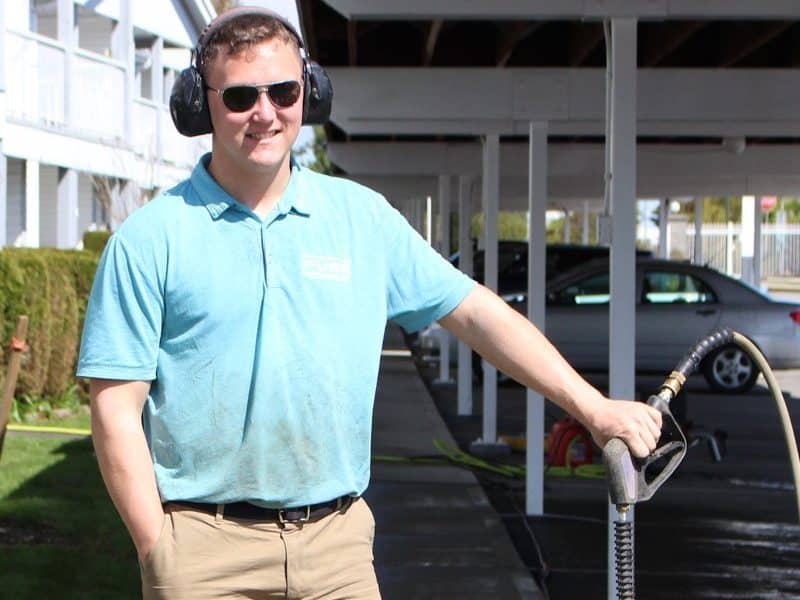 A man from the fuse power washing is holding pressure washers and wearing sunglasses.